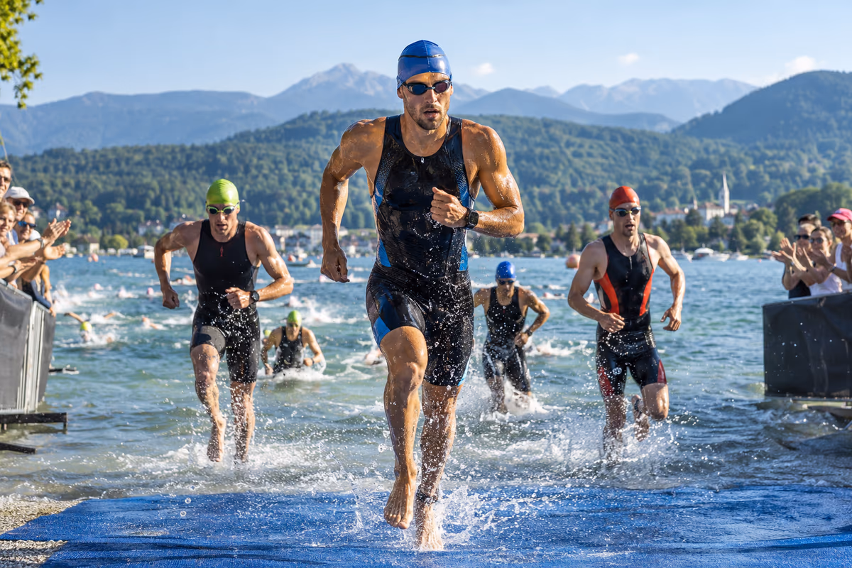 Triathletinnen und Triathleten starten bei Morgenlicht in einen klaren Kärntner Alpensee.